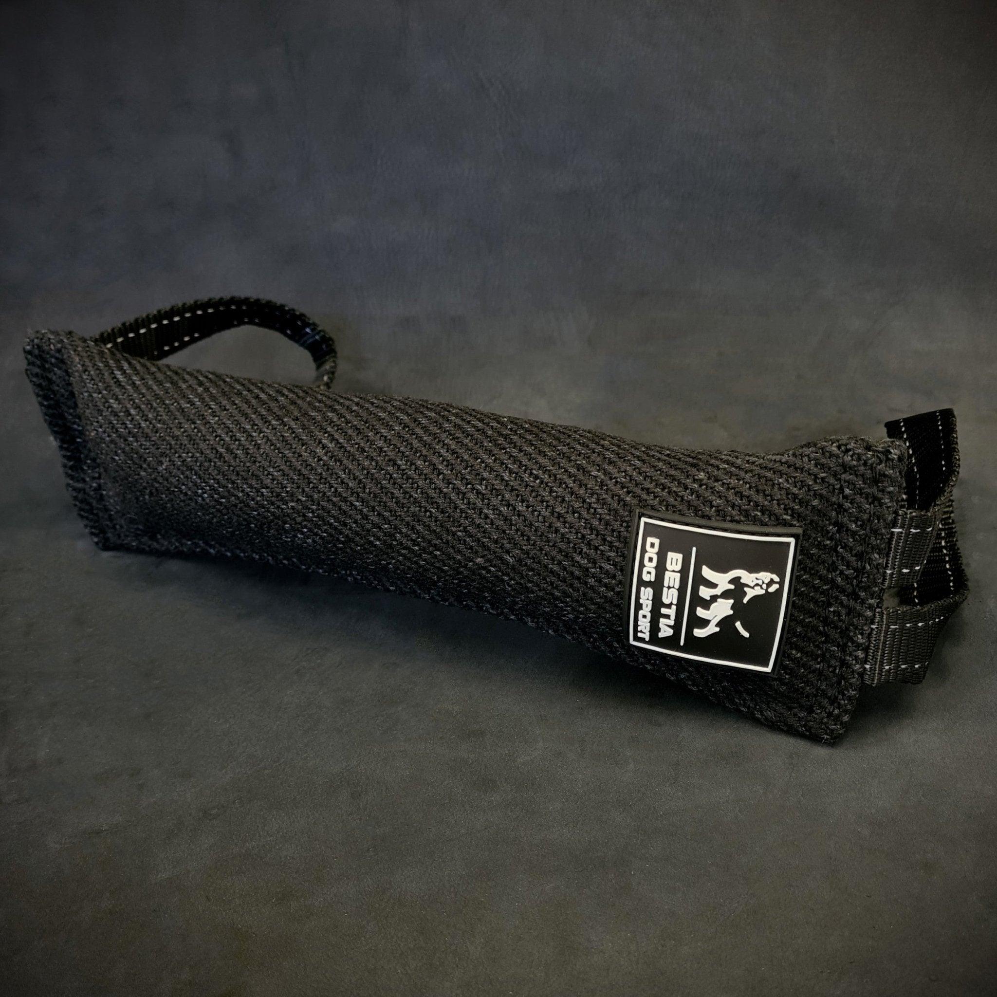 Das BESTIA DOG SPORT – Beißkissen für Hunde von BESTIA DOG SPORT in Schwarz, mit Griff und „Best Dog Gear“-Label, eignet sich perfekt für Biss- und Grifftraining im Hundetraining und wird auf einer dunklen Oberfläche dargestellt.