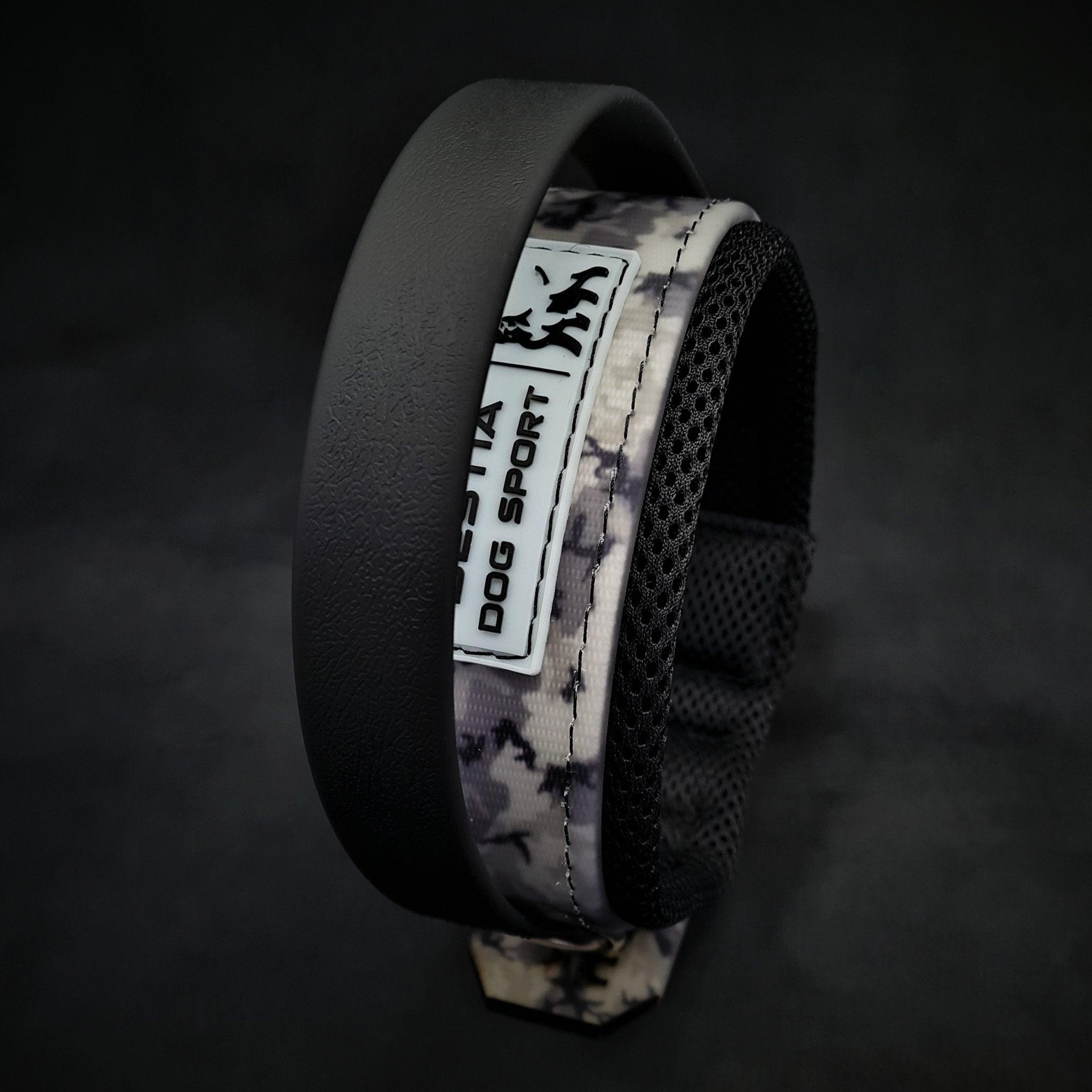 Eine Nahaufnahme des BESTIA DOG SPORT – Handle Halsband Grey Camo von BESTIA DOG SPORT, entworfen für starke Hunderassen, mit einem schwarz gepolsterten Innenfutter und einem „DOG SPORT“-Label auf dunklem Hintergrund.