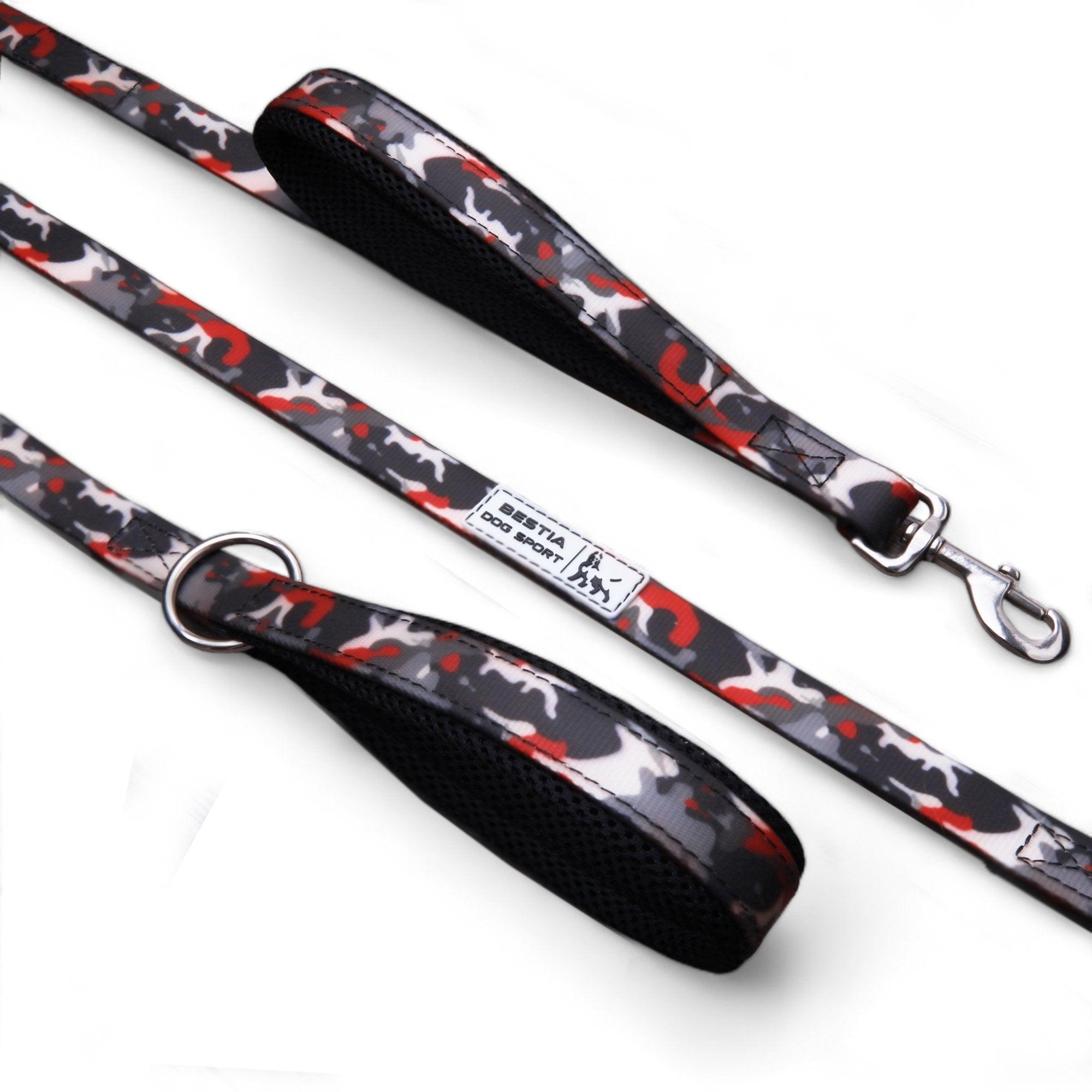 Die BESTIA DOG SPORT – Doppelführleine Red Camo verfügt über einen gepolsterten Griff, einen Metallverschluss und einen D-Ring – perfekt für das Hundetraining. Ihr stilvolles rot-weiß-schwarz-graues Tarnmuster sticht auf weißem Hintergrund hervor.