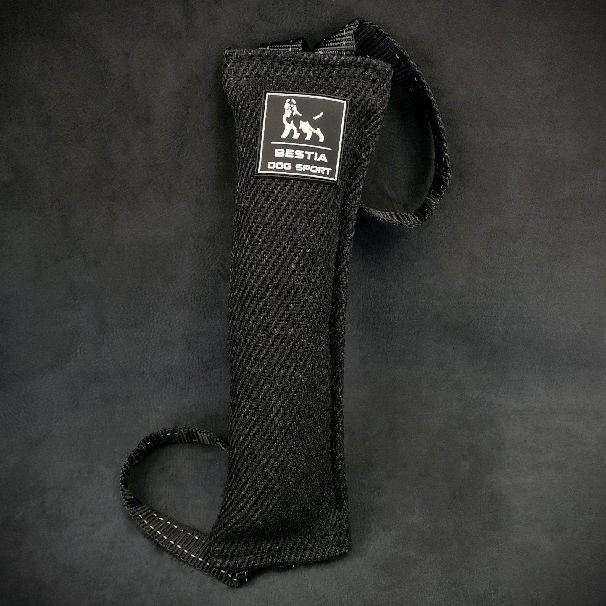 Das BESTIA DOG SPORT – Beißkissen für Hunde von BESTIA DOG SPORT, ideal für Hundetraining und Biss- und Grifftraining, verfügt über ein schwarzes Strukturdesign mit Griff und Logo, dargestellt vor einem schlichten dunklen Hintergrund.