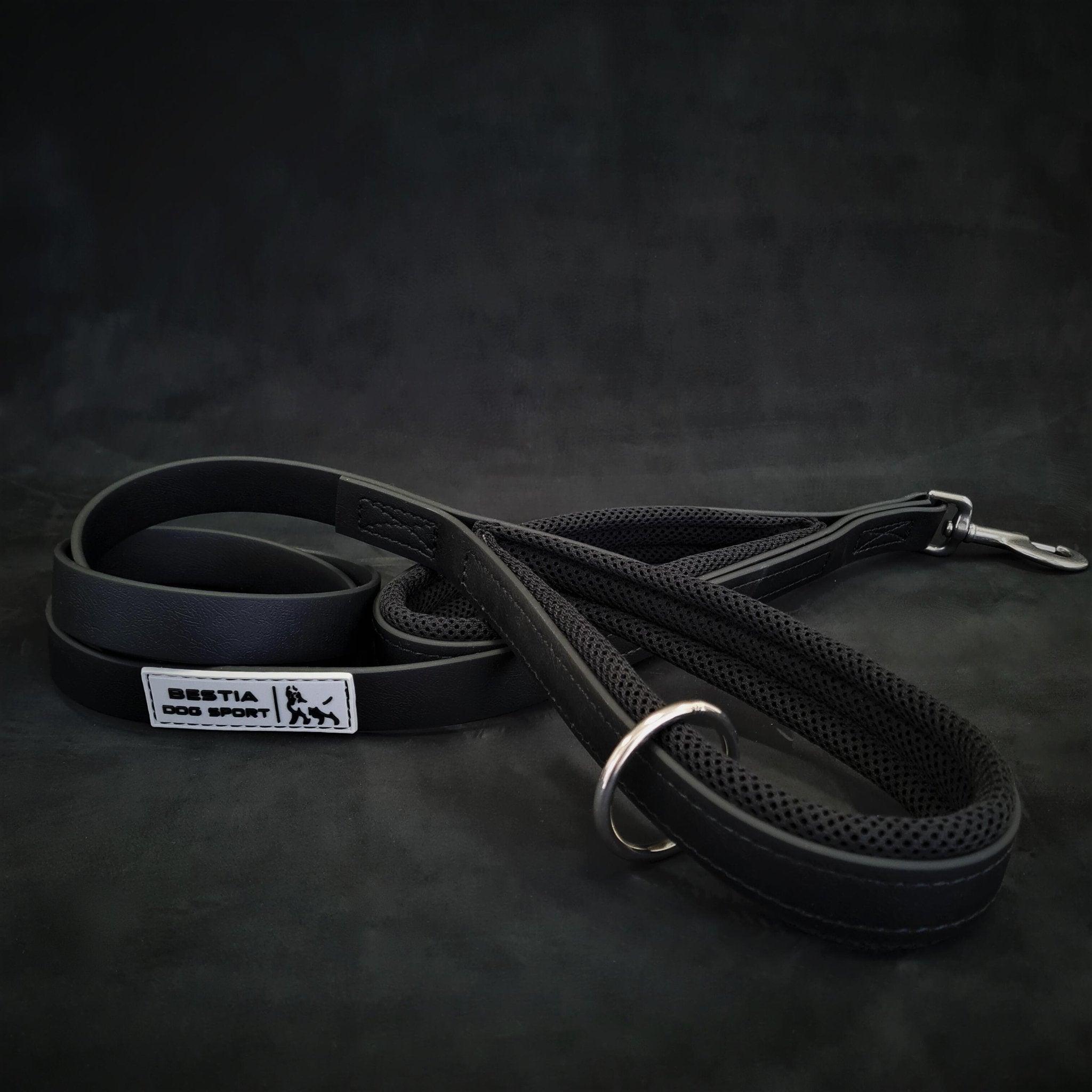 Die BESTIA DOG SPORT – Doppelgriff-Leine Schwarz, featuring zwei gepolsterte Griffe, Edelstahl Karabiner, Metal D-Ring und einem „Bestia Dog Sport“-Label, wird vor dunklem Hintergrund präsentiert.
