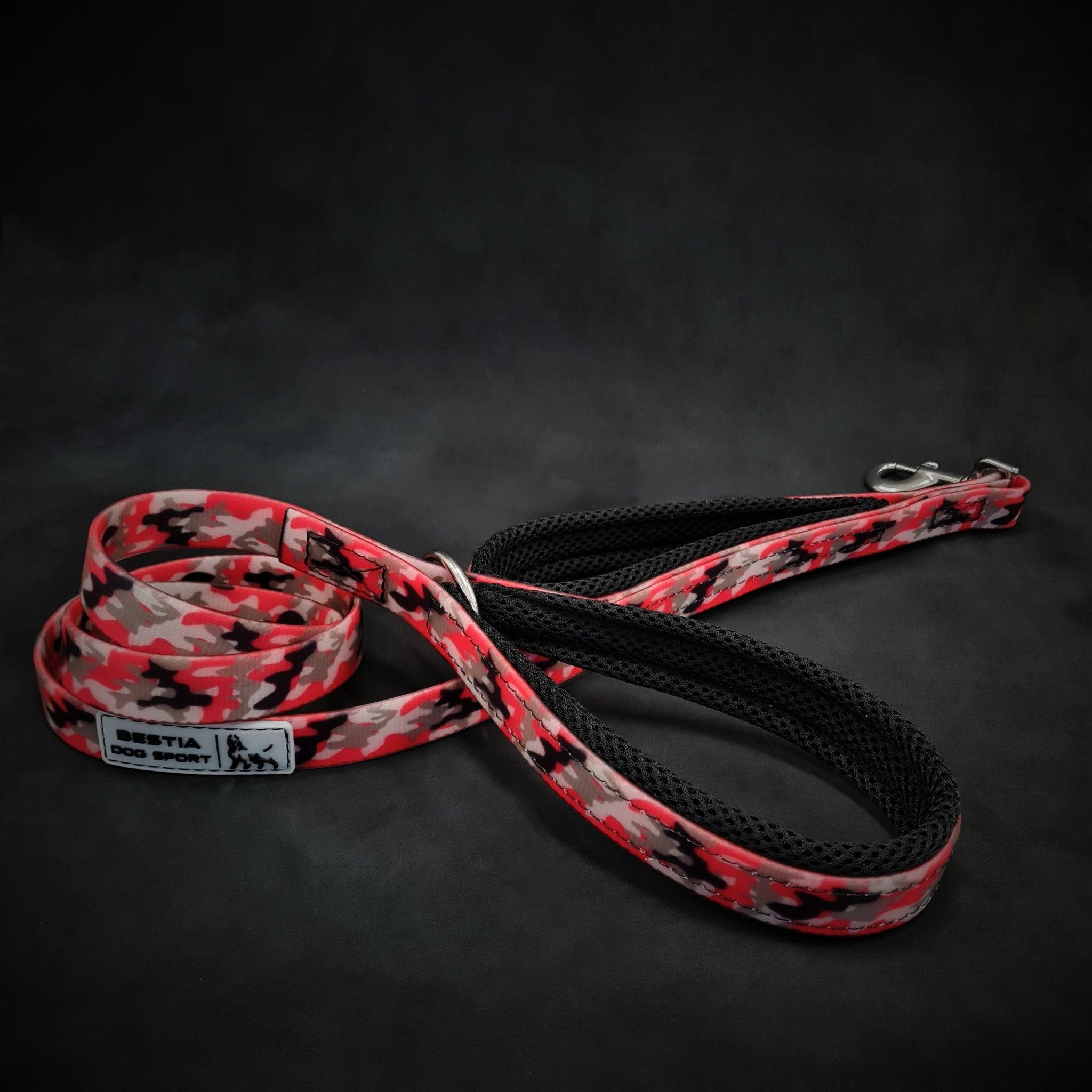 Die BESTIA DOG SPORT – Doppelführleine Red Camo in den Farben Rot, Schwarz und Grau mit Metallclip und Etikett ist ideal für das Hundetraining und auf dunklem Hintergrund abgebildet.