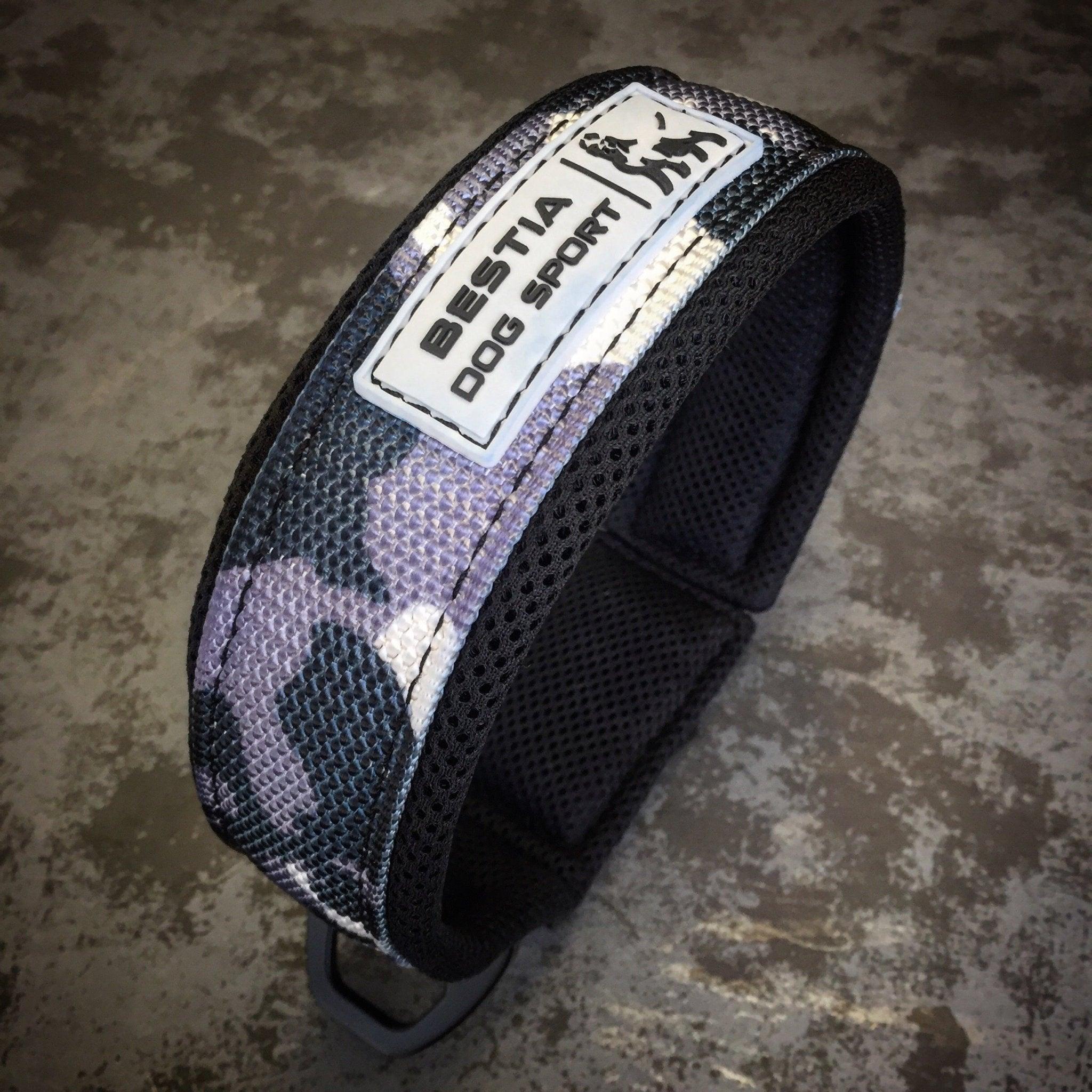 Das BESTIA DOG SPORT – Schnellverschluss-Halsband, camo-gemustert und extrem belastbar für Hundesport, mit „Bestia Dog Sport“ Label, liegt gepolstert auf einer grauen texturierten Oberfläche.