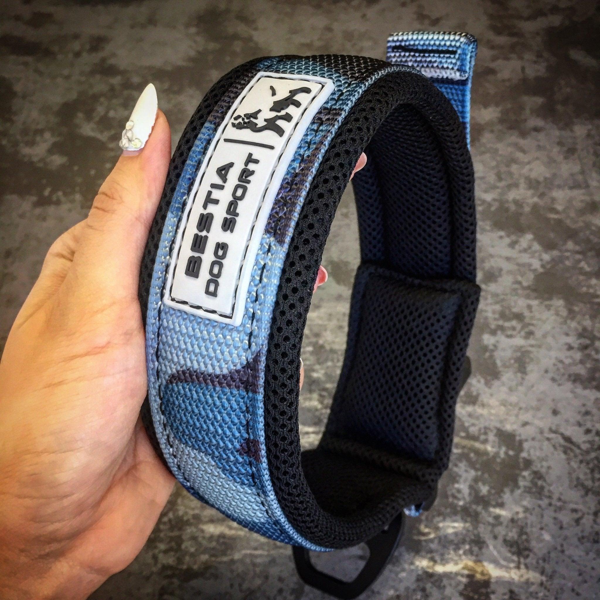 Eine Hand hält das BESTIA DOG SPORT – Schnellverschluss-Halsband Blue Camo-Halsband mit sichtbarem Branding vor einem strukturierten grauen Hintergrund.