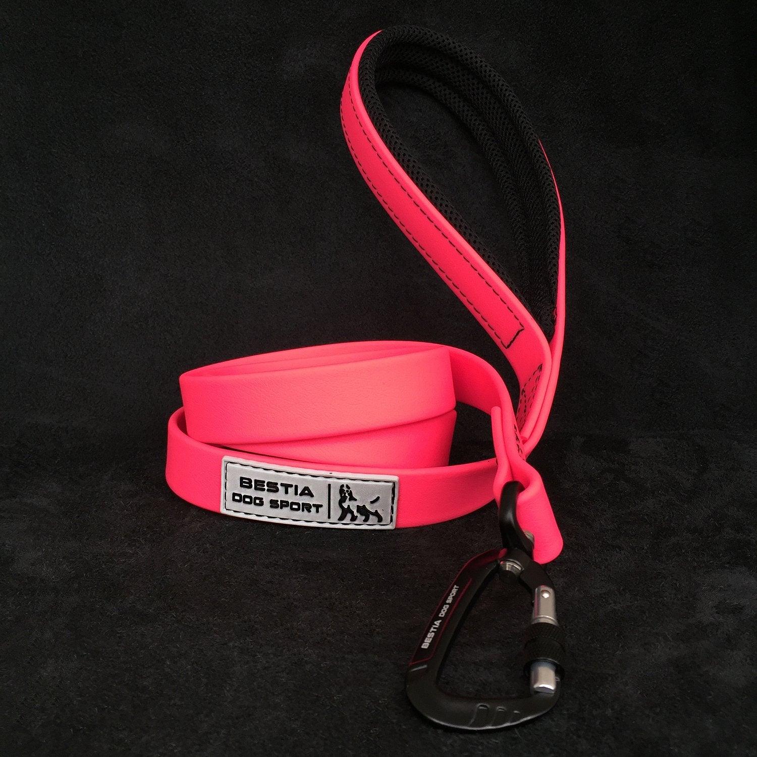 Die BESTIA DOG SPORT – Taktische Leine Neon Pink verfügt über einen gepolsterten Griff, einen stabilen Karabinerhaken aus Metall und das BESTIA DOG SPORT-Logo auf schwarzem Hintergrund.