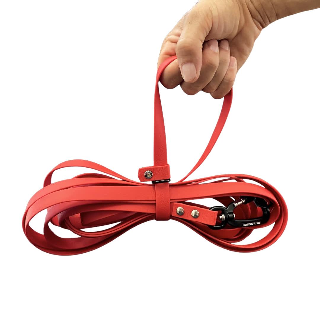 Eine Hand hält die BESTIA DOG SPORT Multifunktions-Schleppleine 5m in Rot mit Metallnieten und Aluminiumkarabiner vor weißem Hintergrund.
